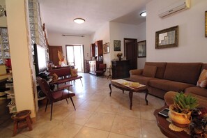 A living room with a brown sofa, a wooden coffee table, and a TV. There is a kitchen area with cabinets and a refrigerator. - L' Oleandro - Key to Villas (Valledoria)