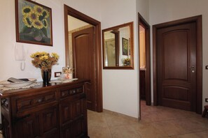 A hallway with a wooden dresser, a vase of sunflowers, a telephone, and a mirror reflecting a door. - L' Oleandro - Key to Villas (Valledoria)
