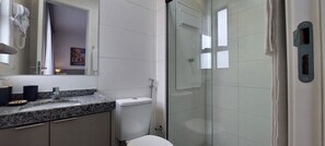 Ein Badezimmer mit Granitplatte, Toilette, Duschkabine aus Glas und Waschbecken in Weiß.