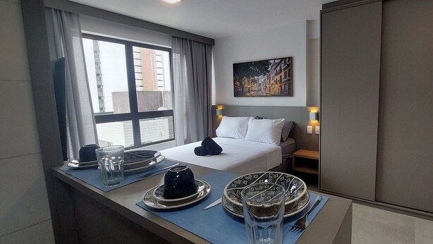 Une chambre d’hôtel avec un lit, une table de chevet, une fenêtre avec des rideaux, un tableau et un miroir.