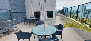 Eine Dachterrasse mit Außenmöbeln, einem Glastisch und Blick auf die Stadtlandschaft.