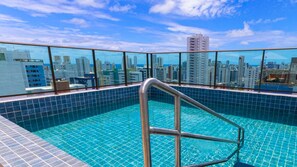 Ein Pool auf dem Dach mit Blick auf die Stadt, einer Metallleiter und gefliesten Rändern.