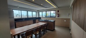 Eine moderne Küche mit einem langen Holztisch und Stühlen, großen Fenstern und einem Feuerlöscher an der Wand.