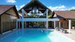 A modern resort with a large pool, outdoor seating, and a covered area with a thatched roof. - Villa Monica: Private retreat near golf w/ staff, pool & golf cart (Punta Cana)