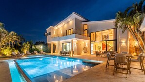 A modern two-story house with a swimming pool, outdoor seating, and palm trees. - Buganvilla Mansion: 2 amazing lakefront villas w/ pools, gym, games, & staff (Punta Cana)