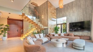 A spacious living room with a modern staircase, a large flat-screen TV, and comfortable seating. - Buganvilla Mansion: 2 amazing lakefront villas w/ pools, gym, games, & staff (Punta Cana)