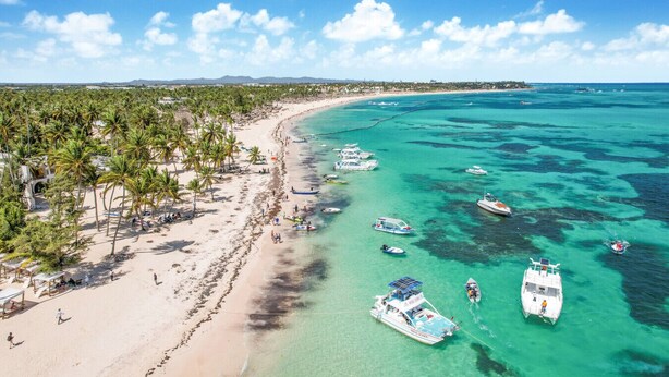 A beach with clear turquoise waters, boats, and palm trees. - Buganvilla Mansion: 2 amazing lakefront villas w/ pools, gym, games, & staff (Punta Cana)