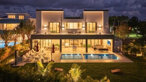 Une maison moderne à deux étages, dotée d’une piscine, d’un espace extérieur aménagé et d’un patio bien éclairé.