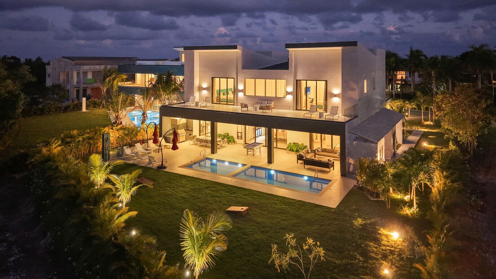 Une maison moderne à deux étages, dotée d’une piscine, d’un espace extérieur aménagé et d’un patio bien éclairé.