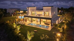 Une maison moderne à deux étages, dotée d’une piscine, d’un espace extérieur aménagé et d’un patio bien éclairé.