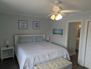 A bedroom with a bed, a nightstand, a ceiling fan, and artwork on the walls. - Pineapple Under The Sea (Carolina Beach)