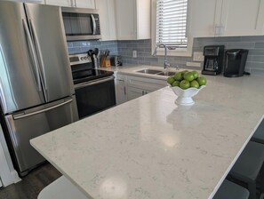 A modern kitchen with stainless steel appliances, a marble countertop, and a bowl of green apples. - Pineapple Under The Sea (Carolina Beach)