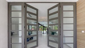 A modern interior with a central staircase, glass doors, and a neutral color scheme. - Las Palmas 3: Luxury retreat w/ pool, Jacuzzi, games, golf carts & full staff (Punta Cana)
