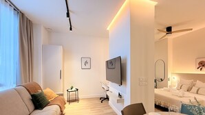 Quarto de hotel moderno com sofá, mesa de jantar, TV e ventoinha no teto.