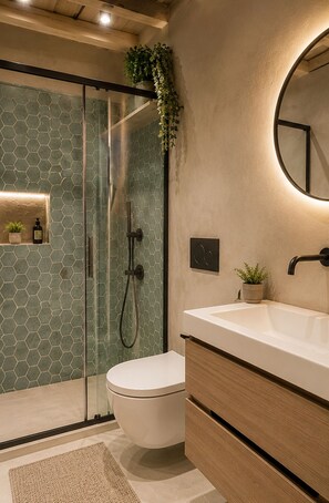Une salle de bain avec une douche à parois de verre, des toilettes blanches, un meuble-lavabo en bois et un miroir rond.