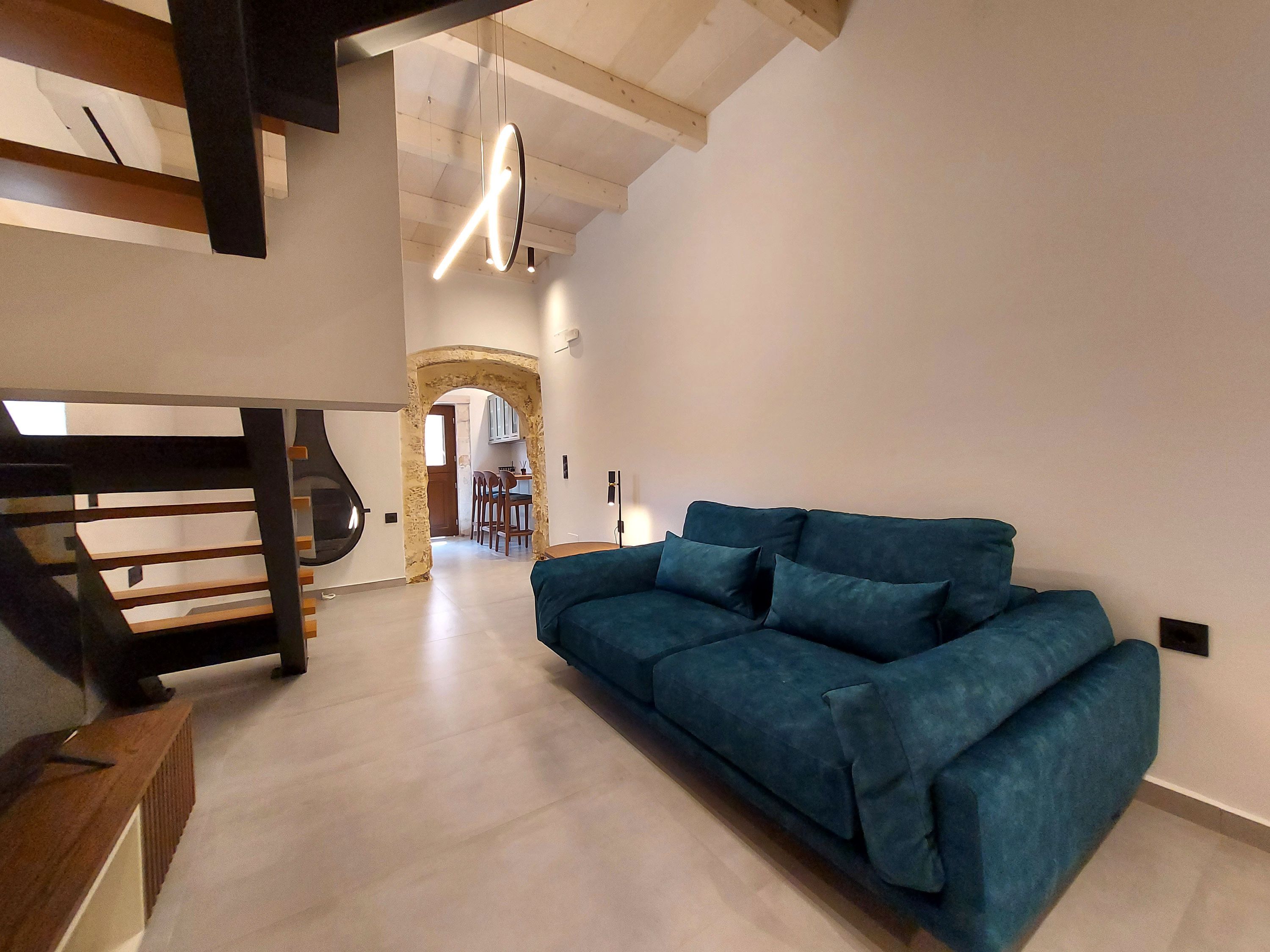 Un salon moderne avec un canapé bleu, un escalier en bois et une cuisine en arrière-plan.