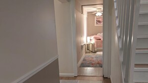Un pasillo que conduce a un dormitorio con cama, mesita de noche y ventilador de techo.