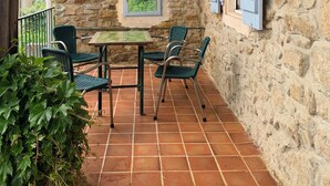 A stone-walled patio with a table and chairs, a window, and a view of greenery. - Fine vacation home in mountain village; endless hiking, cycling and MTB possibilities (Saint-Gervais-sur-Mare)