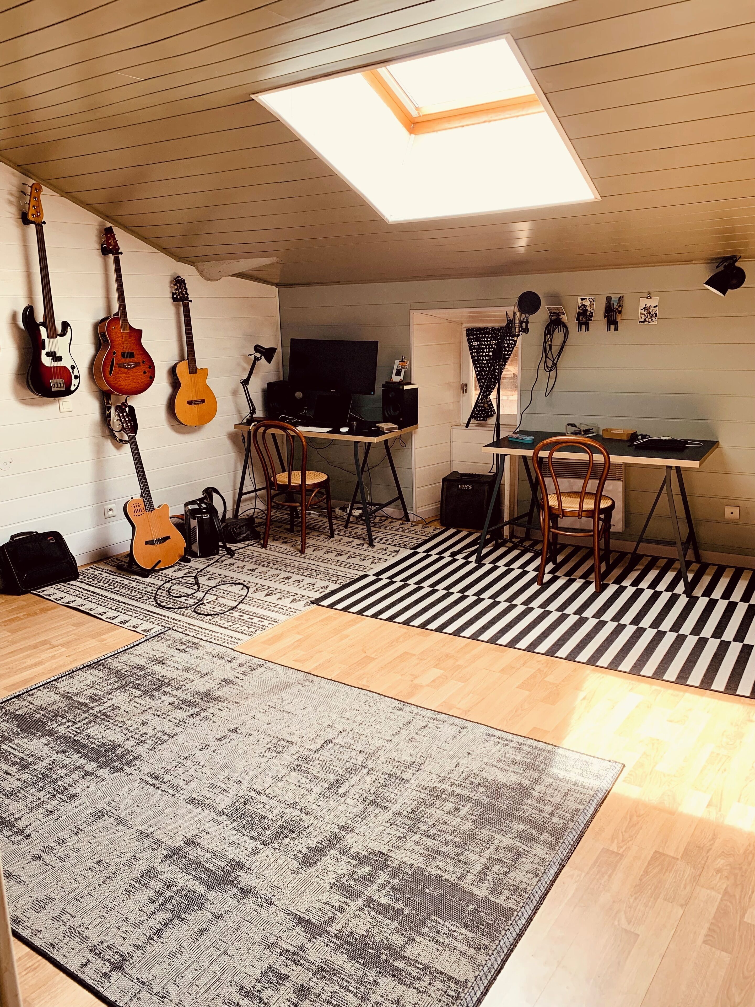 A room with a skylight, a desk with a computer, a chair, and several guitars on the wall.