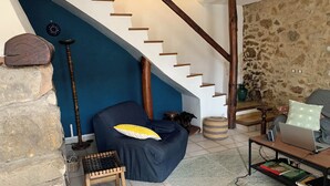 A living room with a blue wall, a wooden staircase, a stone wall, a dog, a chair, a table with a laptop, and a bookshelf. - Fine vacation home in mountain village; endless hiking, cycling and MTB possibilities (Saint-Gervais-sur-Mare)