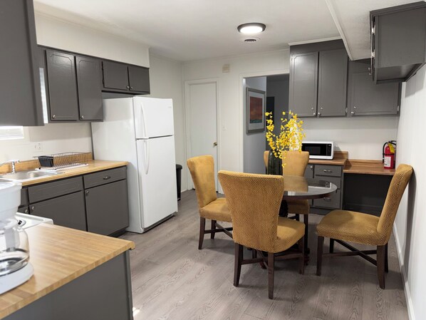 Una cocina moderna con armarios grises, un refrigerador blanco, una mesa de comedor de madera con cuatro sillas y un jarrón con flores amarillas.