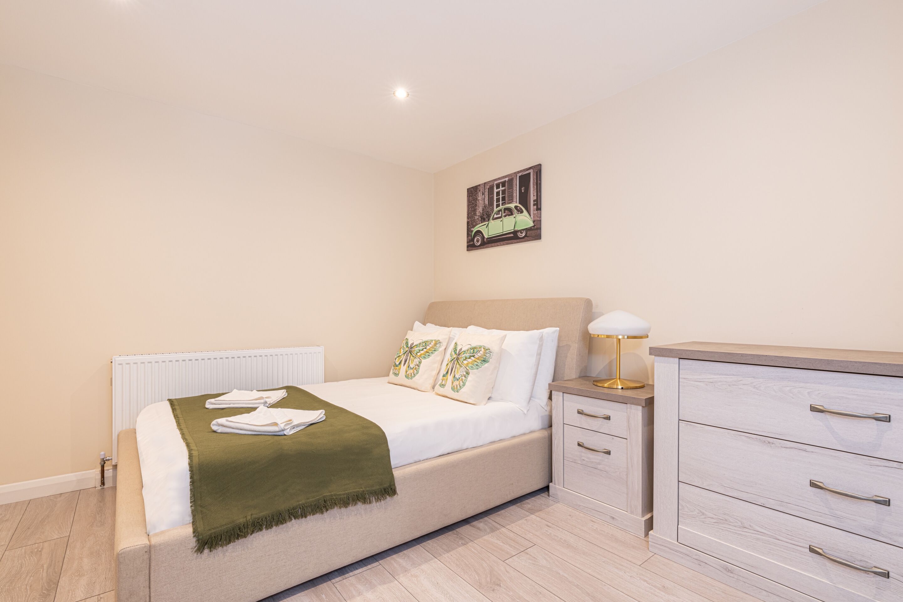 A bedroom with a bed, bedside table, lamp, and a dresser.