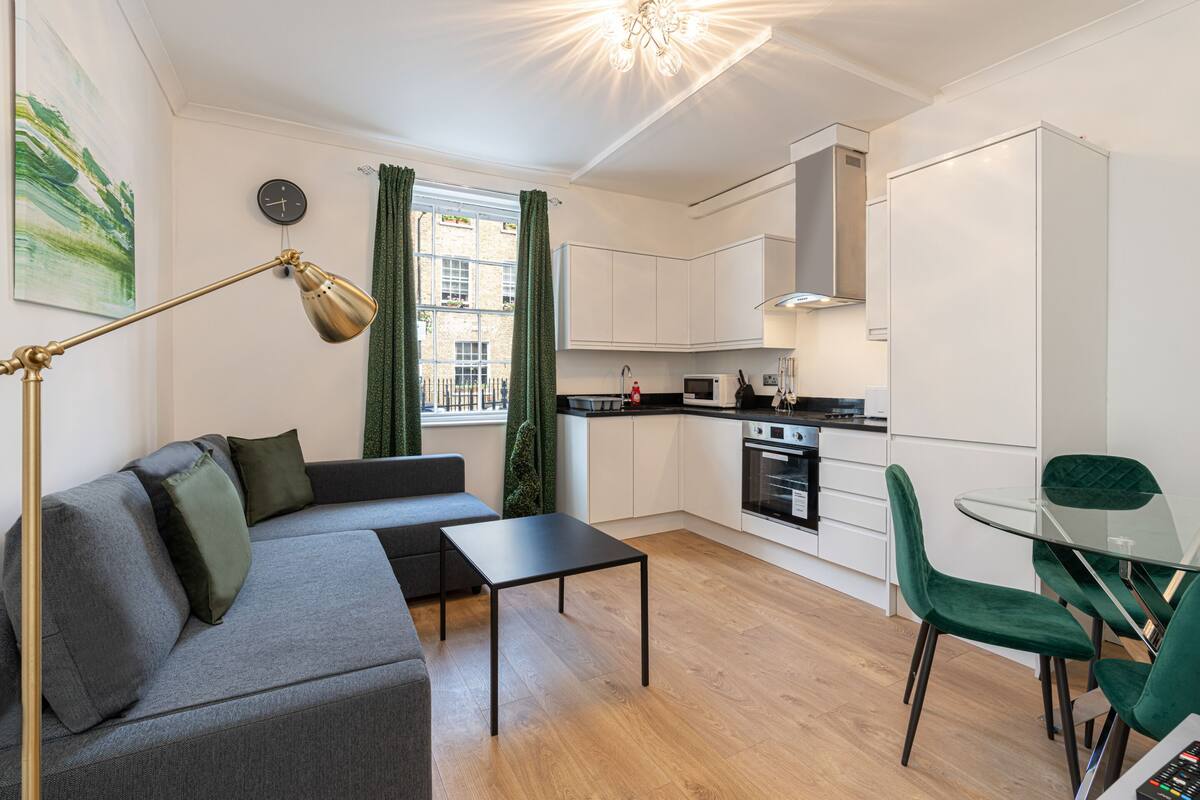 Een moderne keuken met witte kasten, een eettafel met groene stoelen, een bank met kussens en een vloerlamp.