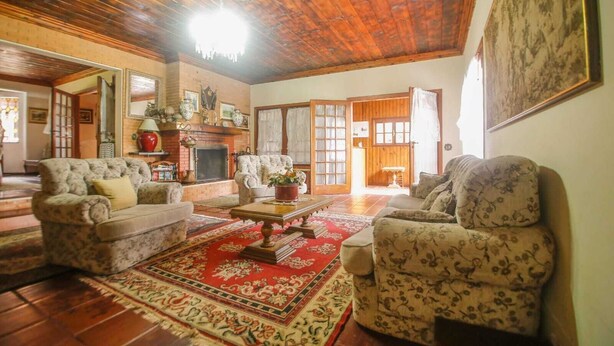 Una sala de estar acogedora con chimenea, dos sillones, una mesita de centro y un tapete rojo estampado.