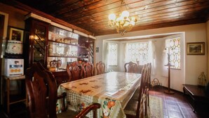 Comedor con mesa de madera, sillas y una araña. Se ven ventanas con vidrio decorativo y un aparador con puertas de cristal.