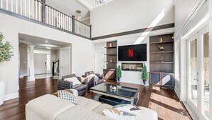 A spacious living room with a high ceiling, a staircase, and a large TV mounted on the wall. - Sunnymede Vacation Stay (Richmond)