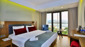 Ein Hotelzimmer mit Bett, Schreibtisch, Stuhl und Blick auf eine Skyline durch große Fenster.