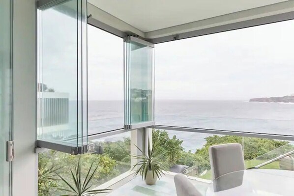 Une chambre moderne dotée d’une grande baie vitrée offrant une vue sur la mer et le paysage lointain.
