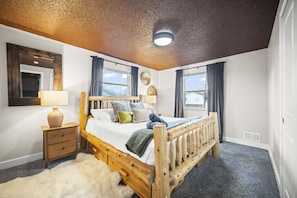 Een slaapkamer met een houten bed, nachtkastje, lamp, een vachtkleed en een plafondlamp.