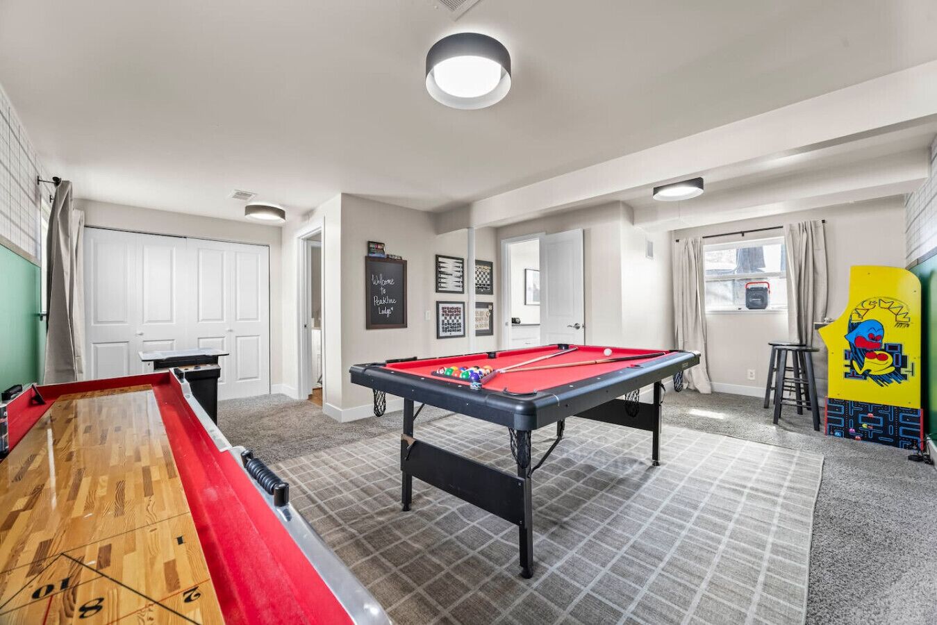 A pool table with a red felt top, a shuffleboard table, and a billiards table in a room with a tiled floor and white walls.