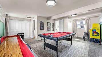 A pool table with a red felt top, a shuffleboard table, and a billiards table in a room with a tiled floor and white walls.