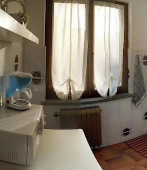 Une cuisine équipée d’un four à micro-ondes, d’une bouilloire et d’une fenêtre avec des rideaux.