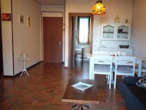 Un salon avec un plancher en bois, une table basse, un canapé blanc et un coin repas comprenant une table et des chaises.