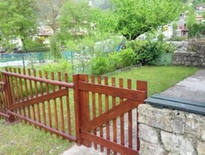 Une porte en bois qui mène à un mur de pierres, le tout entouré de verdure et sous un ciel dégagé.