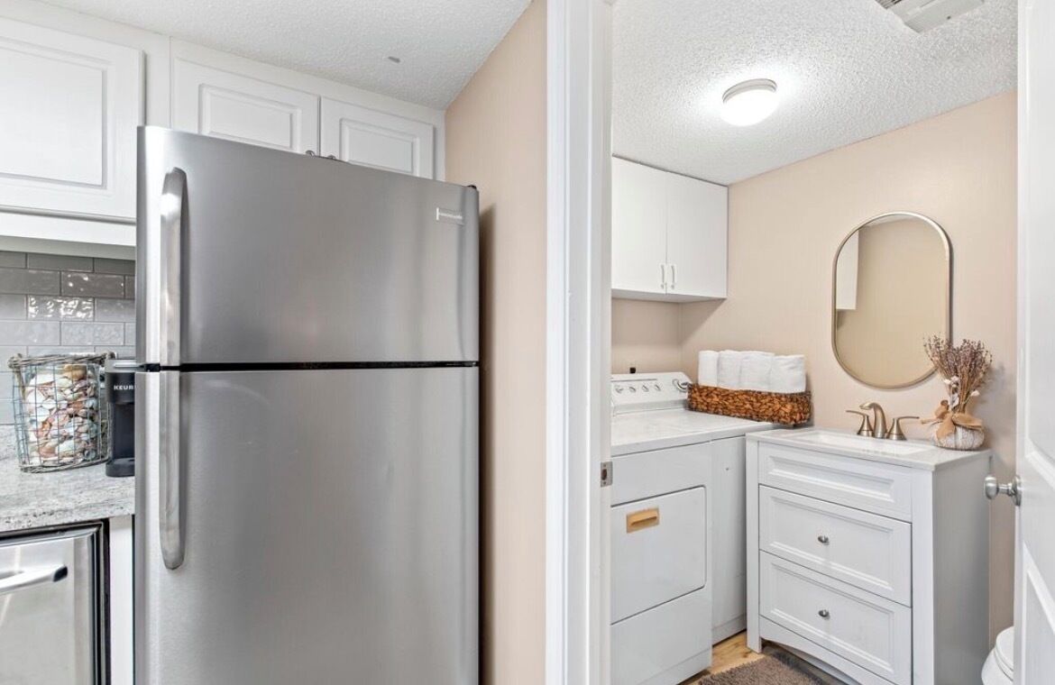 A modern kitchen with white cabinets, a stainless steel refrigerator, and a small countertop with a sink and decorative items.