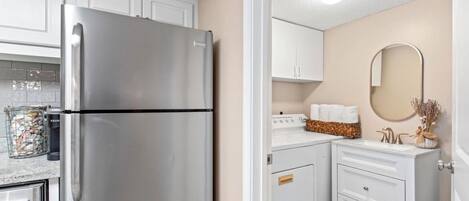 A modern kitchen with white cabinets, a stainless steel refrigerator, and a small countertop with a sink and decorative items.