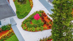 Eine Vogelperspektive auf eine angelegte Grünfläche mit abgetrennten Blumenbeeten und einem zentralen Baum.