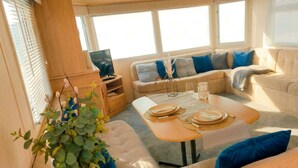 A cozy RV interior with a sofa, dining table, and a television. - North Wales Coastal Stay 2 (Rhyl)