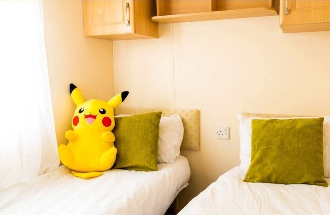A room with two beds, each with a pillow and a Pikachu plush toy.