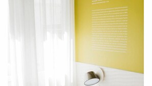 Una camera da letto con un letto, tende bianche e una parete gialla con testo.