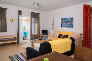 Un salon moderne avec un canapé, une table basse et un téléviseur. On y trouve une porte avec des volets rouges et un tableau accroché au mur.