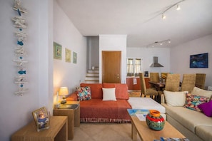 Una habitación acogedora con sofá, una mesita y una silla. Una escalera conduce a otra habitación.