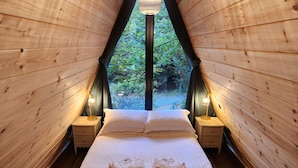 Ein gemütlicher Holzraum mit einem Bett, zwei Nachttischen und Blick ins Grüne.