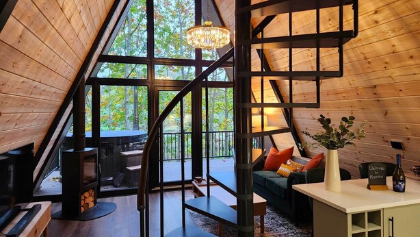 Ein gemütliches, hölzernes Interieur mit einer Treppe zu einem Balkon, einem Kamin und einer Sitzecke mit Kissen.
