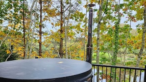 Ein Grill auf einer Holzterrasse mit Blick auf einen See und Herbstbäume.