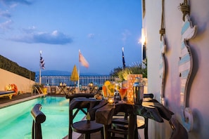 A poolside area with a table set for dining, a cocktail shaker, and a view of the sea.